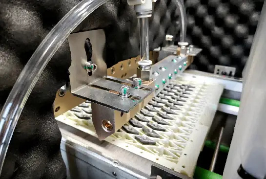 Wet blasting nozzles above a tray of cutting inserts